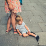 Sad crying toddler sitting in the street by his mother’s feet